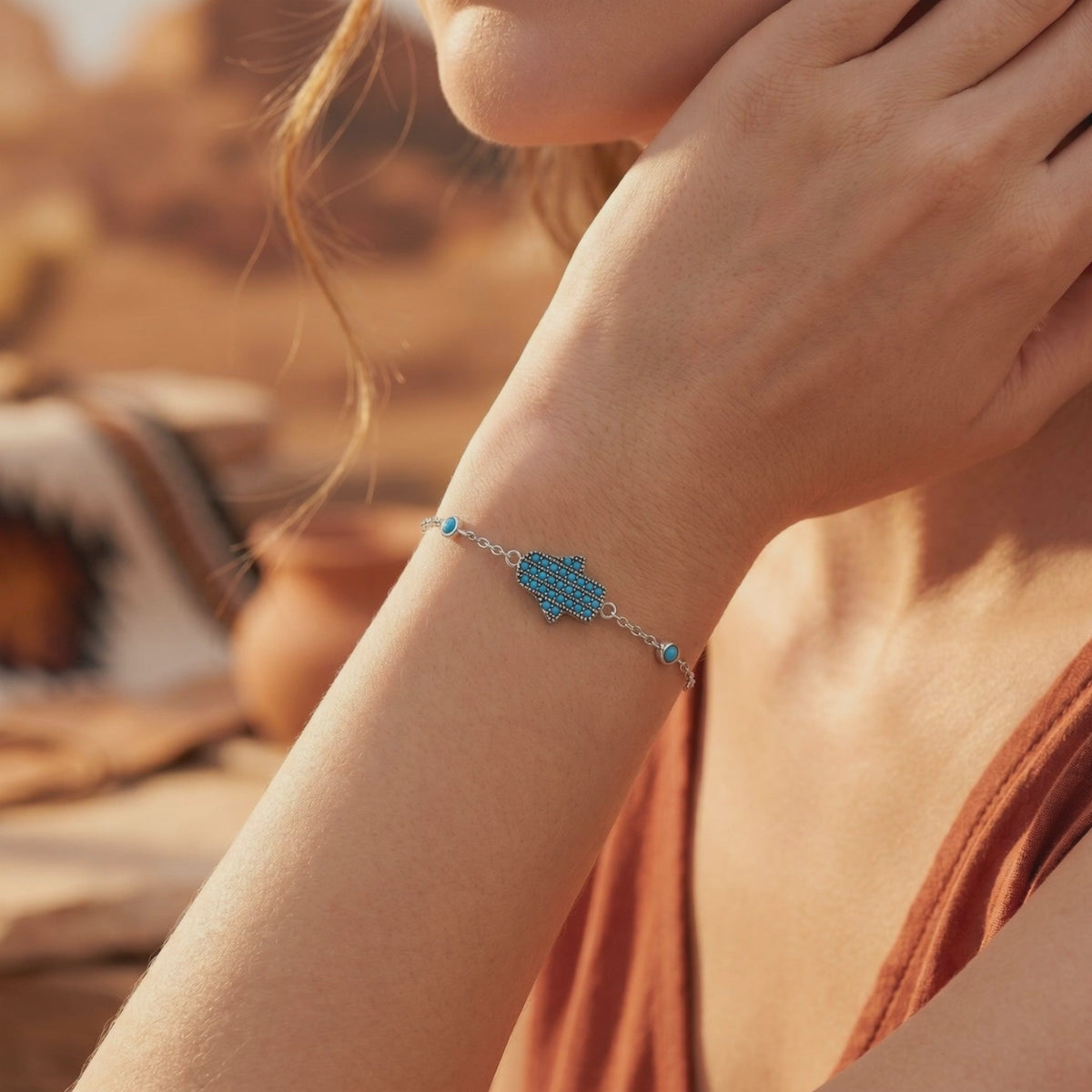 Silver bracelet with a blue-studded Hamsa centerpiece and round turquoise accents worn on a wrist.