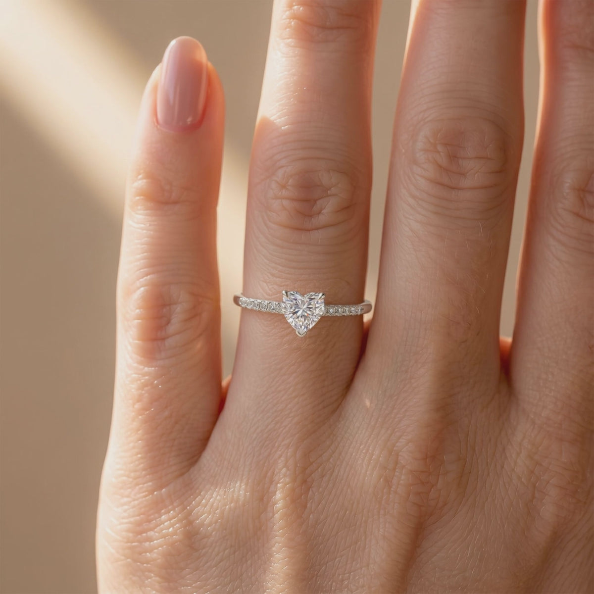 Front view of a silver-colored heart-cut solitaire ring with a pavé band worn on a finger.