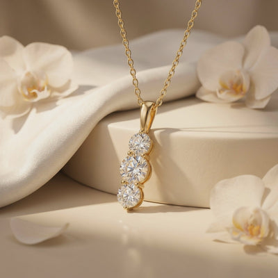 Close-up of a gold-tone necklace with a vertical three-stone pendant displayed among white orchids.