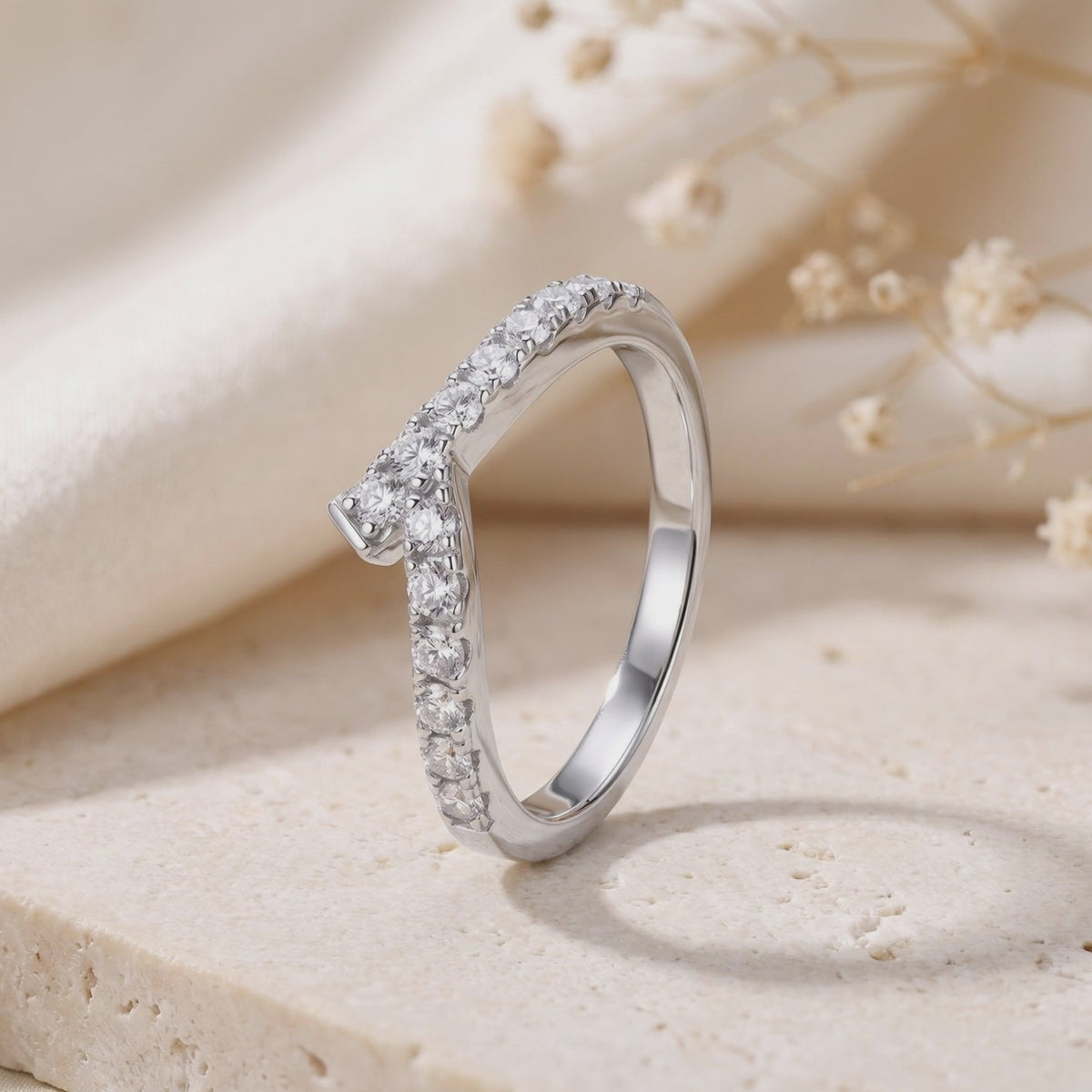 Close-up of a silver asymmetric chevron ring with pave-set stones standing on a textured stone slab.