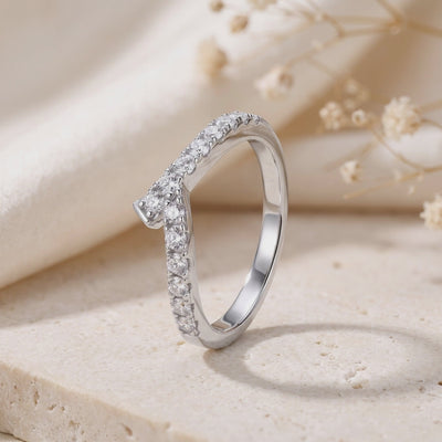 Close-up of a silver asymmetric chevron ring with pave-set stones standing on a textured stone slab.