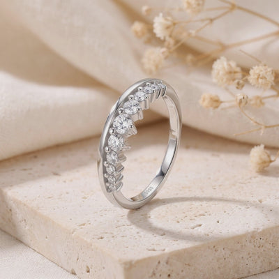 Silver curved ring with graduated clear stones, shown upright on a stone block with S925 stamp visible.