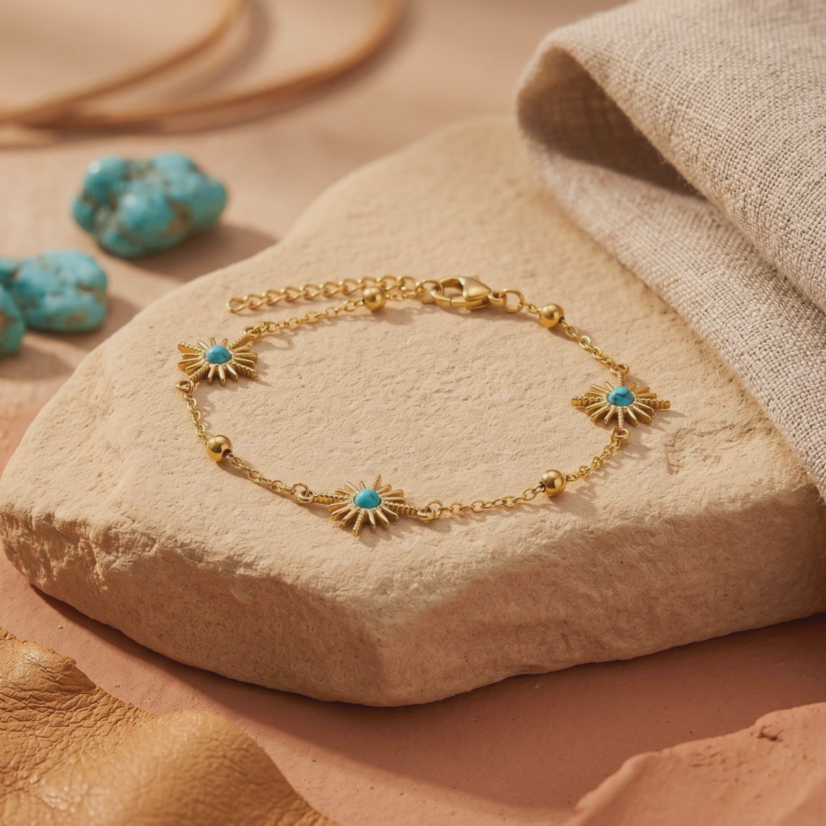 Gold-tone bracelet with three sunburst charms and turquoise-color accents, displayed on a textured stone slab