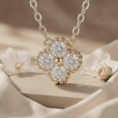 Close-up of a gold-toned clover pendant with four round clear stones and beaded edge details.