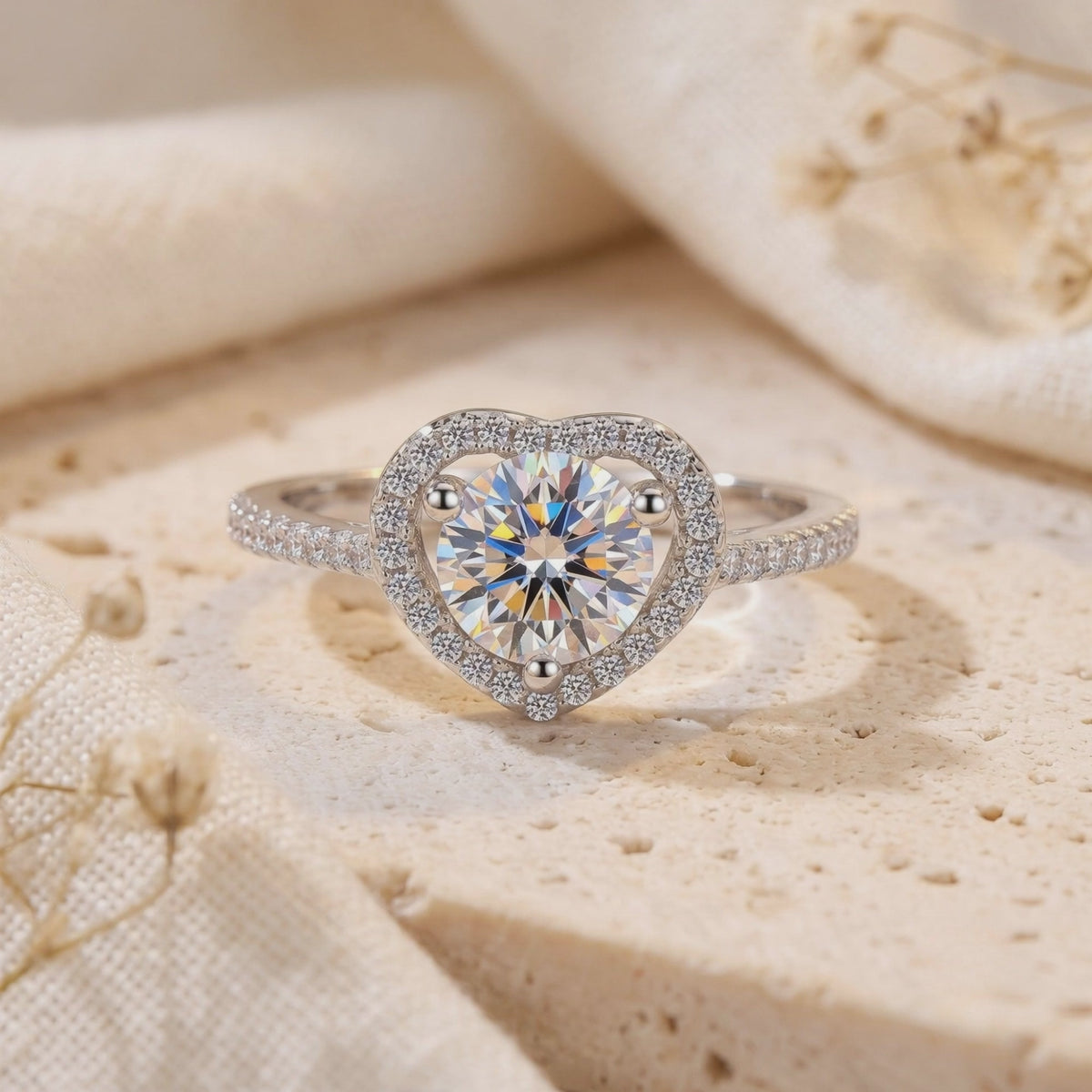 Close-up of a silver ring with a round center stone inside a heart-shaped halo on a textured stone surface.