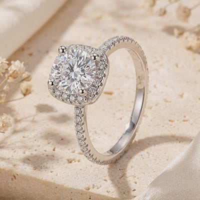 Close-up of the cushion halo ring standing on a stone surface, showing its round center stone and pavé band.