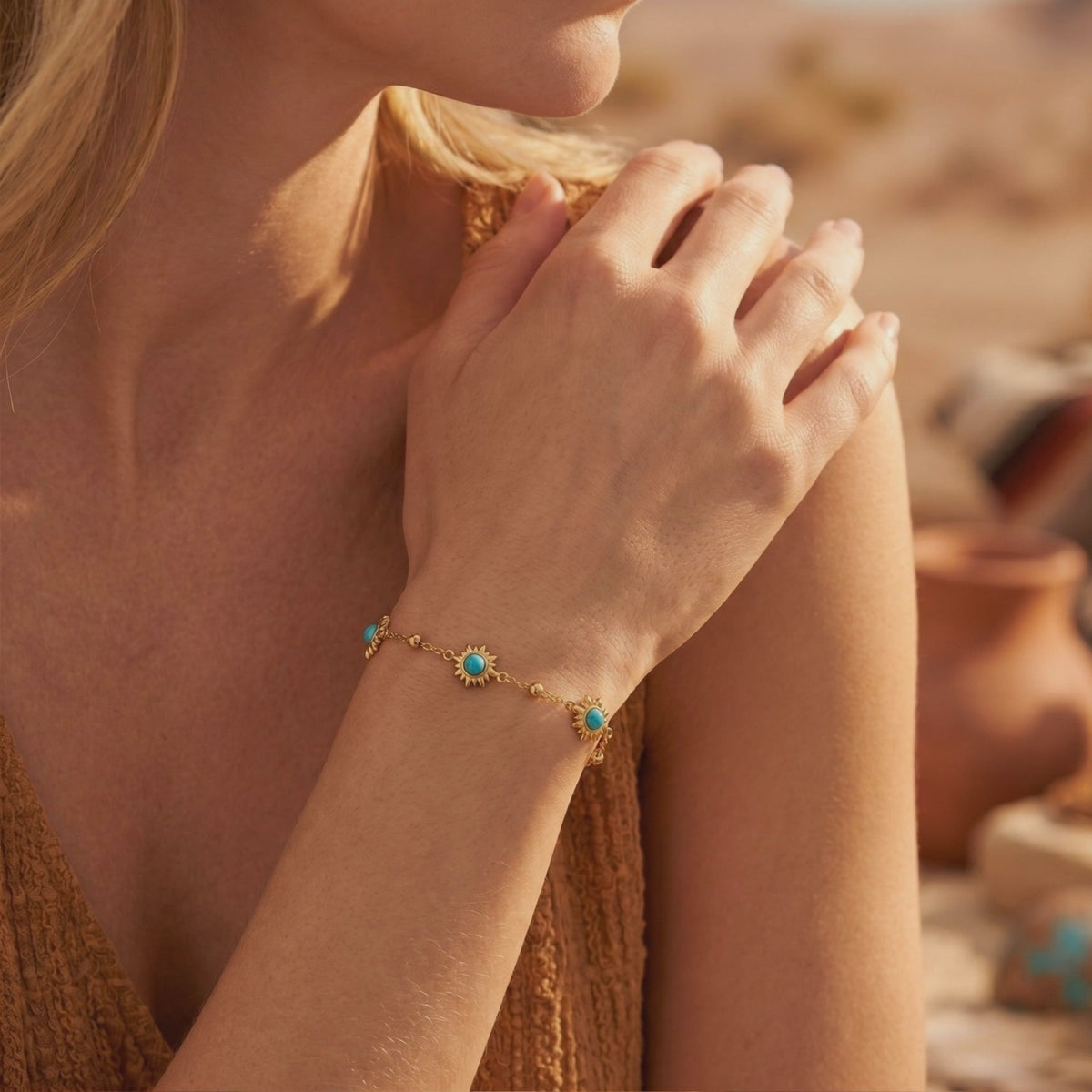 Gold-tone sunburst bracelet with turquoise-hued stones worn on a woman's wrist near her shoulder.