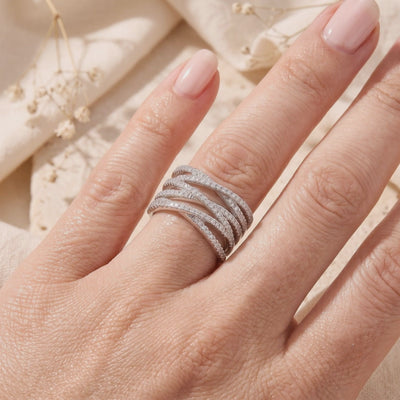 Silver multi-row criss-cross pavé ring worn on a finger against a beige backdrop with dried flowers.