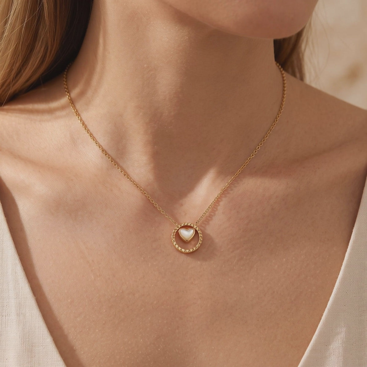 Gold-toned necklace with a circular pendant and mother-of-pearl heart, shown worn on a model’s neckline.