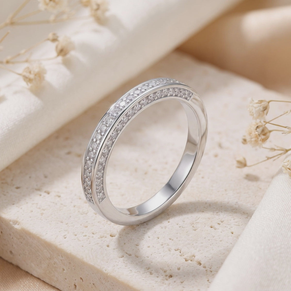Silver double-row pavé band with clear stones, standing upright on a cream stone tile.