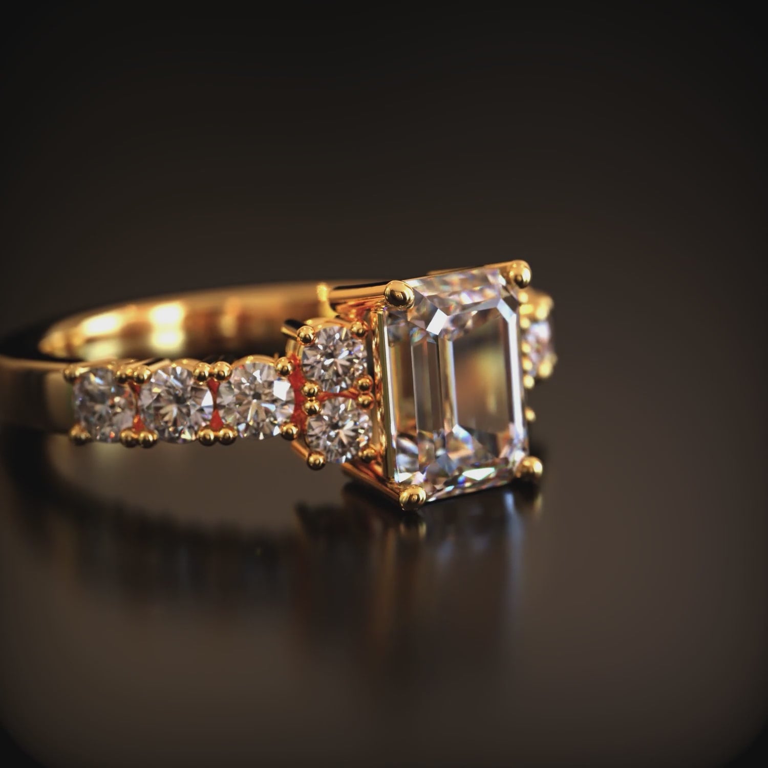 A solid gold ring with an emerald-cut moissanite center stone and pavé side stones.