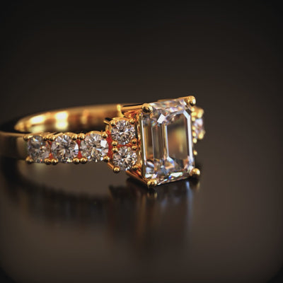 A solid gold ring with an emerald-cut moissanite center stone and pavé side stones.