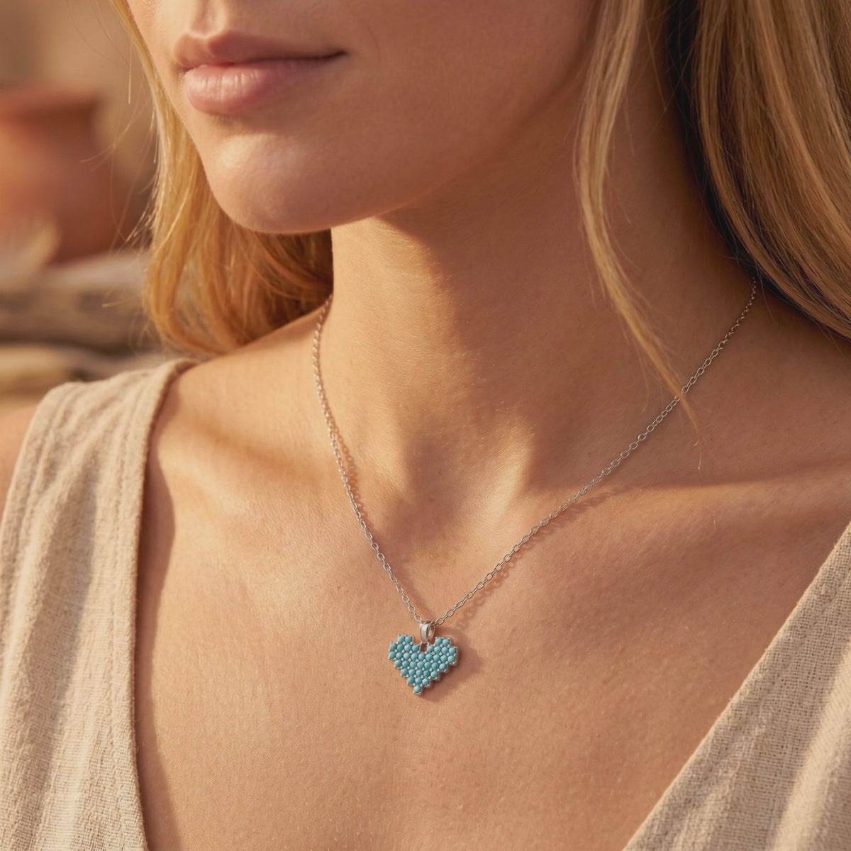 Model wearing a silver chain necklace with a heart pendant made of small blue turquoise stones.