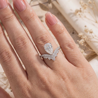 Worn on a hand, a silver wishbone ring shows a pear-cut center stone and nested micro-pavé bands.