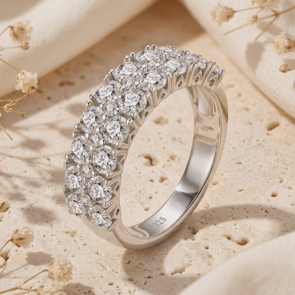 Triple-row silver ring with round cubic zirconia displayed upright on a textured cream surface, showing its S925 hallmark