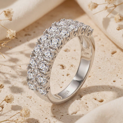 Triple-row silver ring with round cubic zirconia displayed upright on a textured cream surface, showing its S925 hallmark