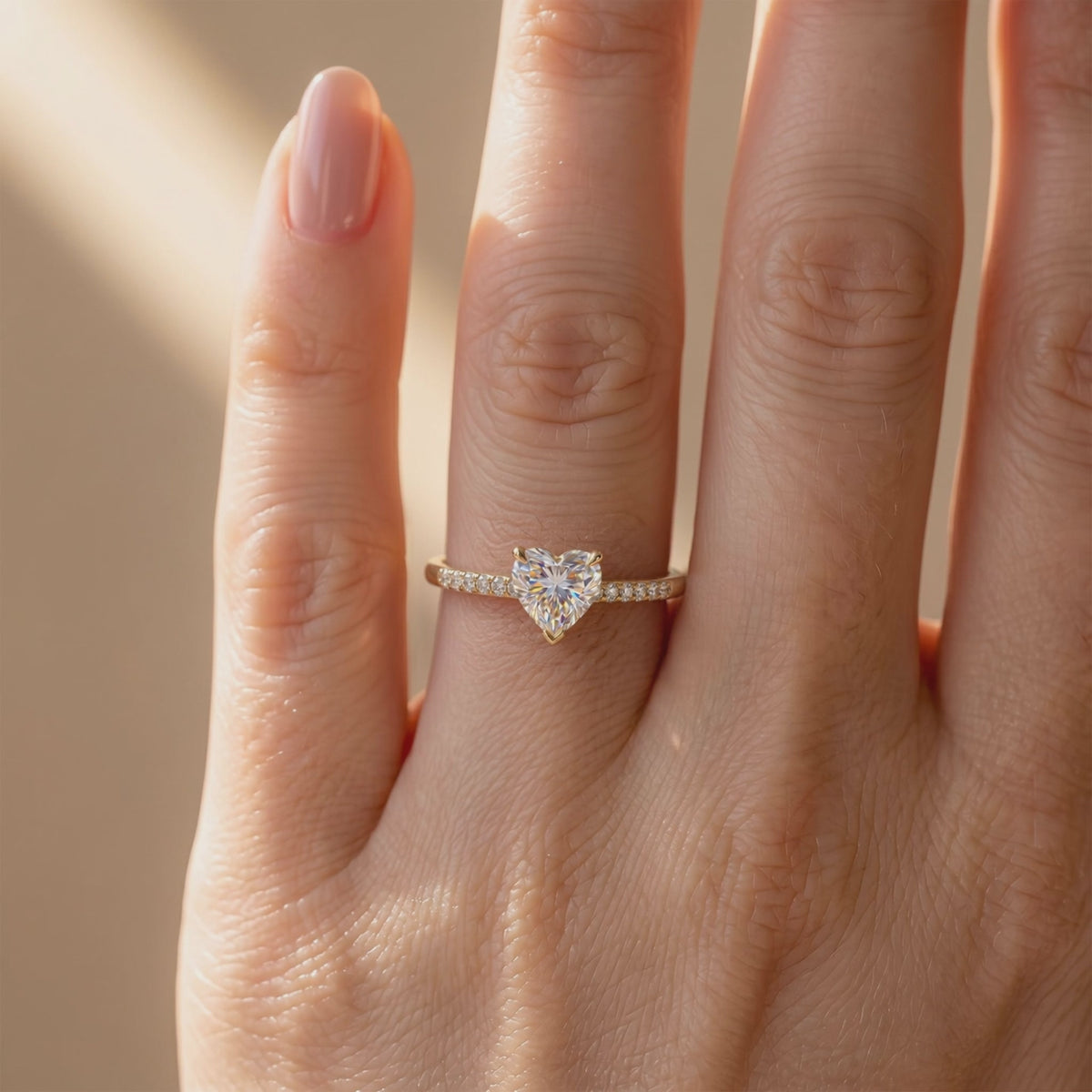 Heart-cut solitaire ring with a pavé yellow gold-toned band, shown worn on a finger.