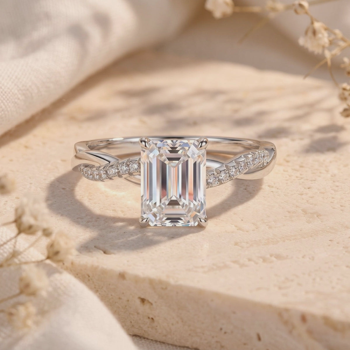 Close-up of a silver emerald-cut solitaire ring with a twisted pavé band on a pale textured surface.