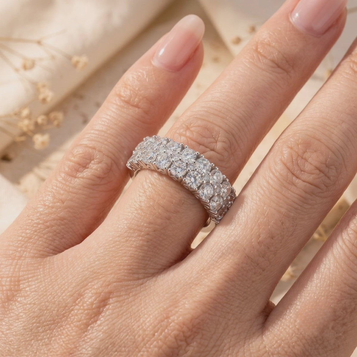Triple-row silver ring with round cubic zirconia worn on a hand against a soft beige floral background