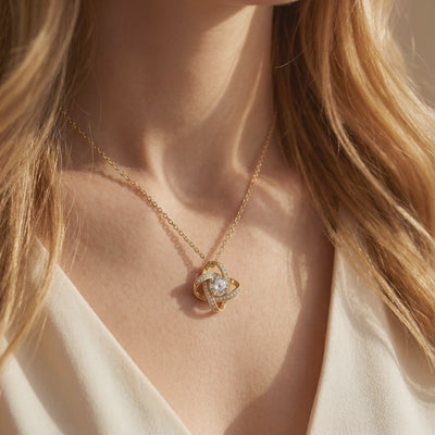Gold interlocking knot necklace with a clear center stone, shown in a close-up while worn on a person's neck.