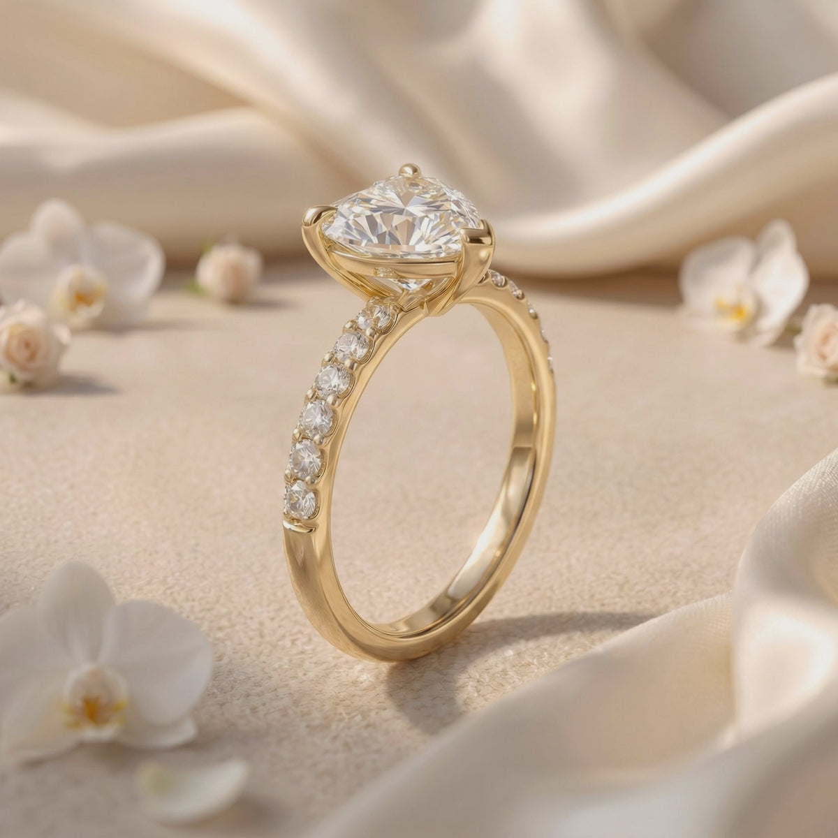 Angled side view of a heart-cut solitaire ring with a pavé band on cream fabric among white flowers.
