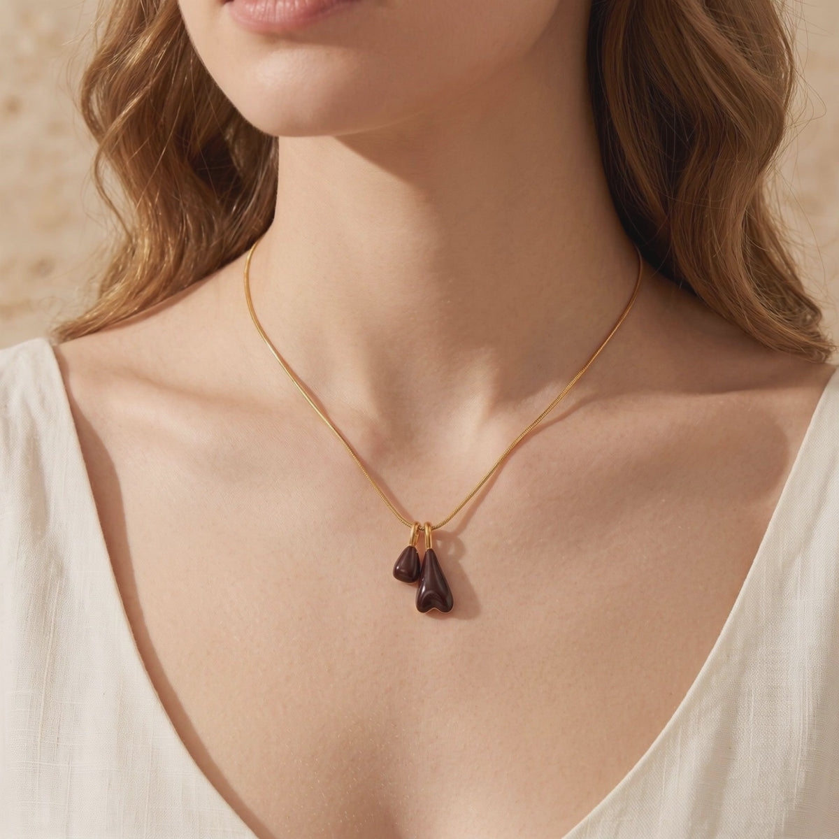 The Marais gold necklace with two glossy burgundy pendant drops worn against a white top.