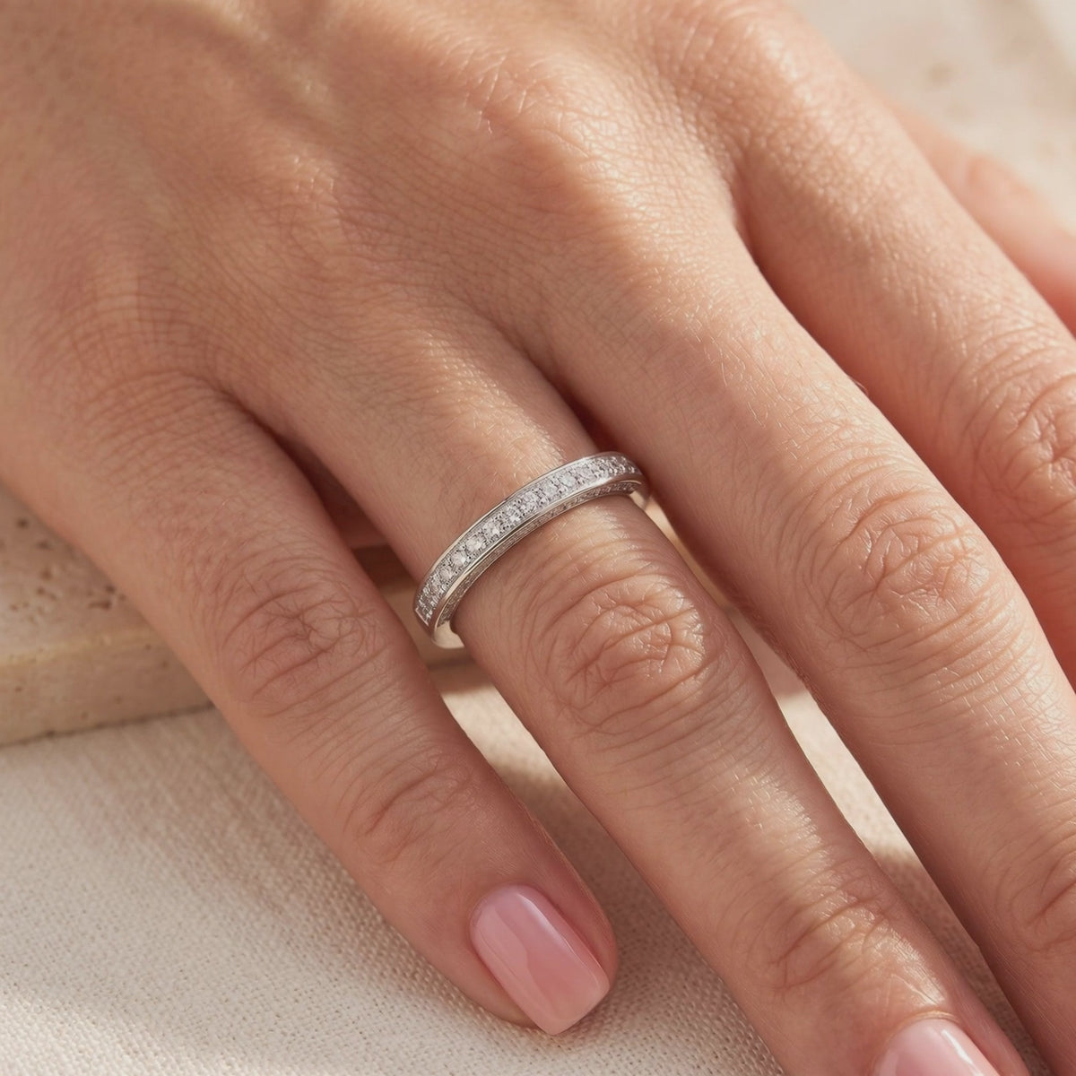 Silver double-row pavé band with small clear stones, shown worn on a person's finger.