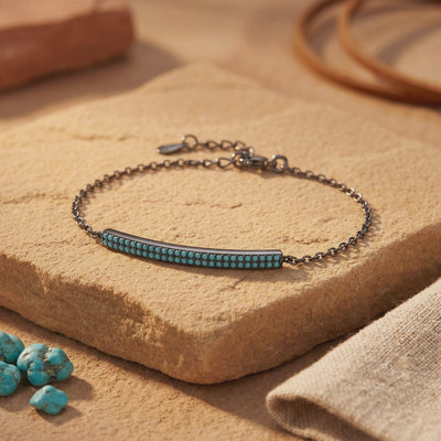Dark silver chain bracelet with a double-row turquoise bar displayed on a tan stone slab.