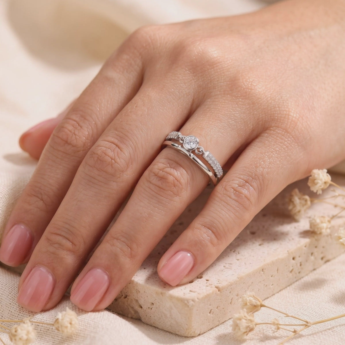 Silver double-band ring worn on a hand, with a round bezel-set center stone and small clear stones on the upper band.