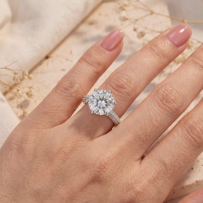 Large round solitaire silver ring with a six-prong setting and pavé band worn on a hand.
