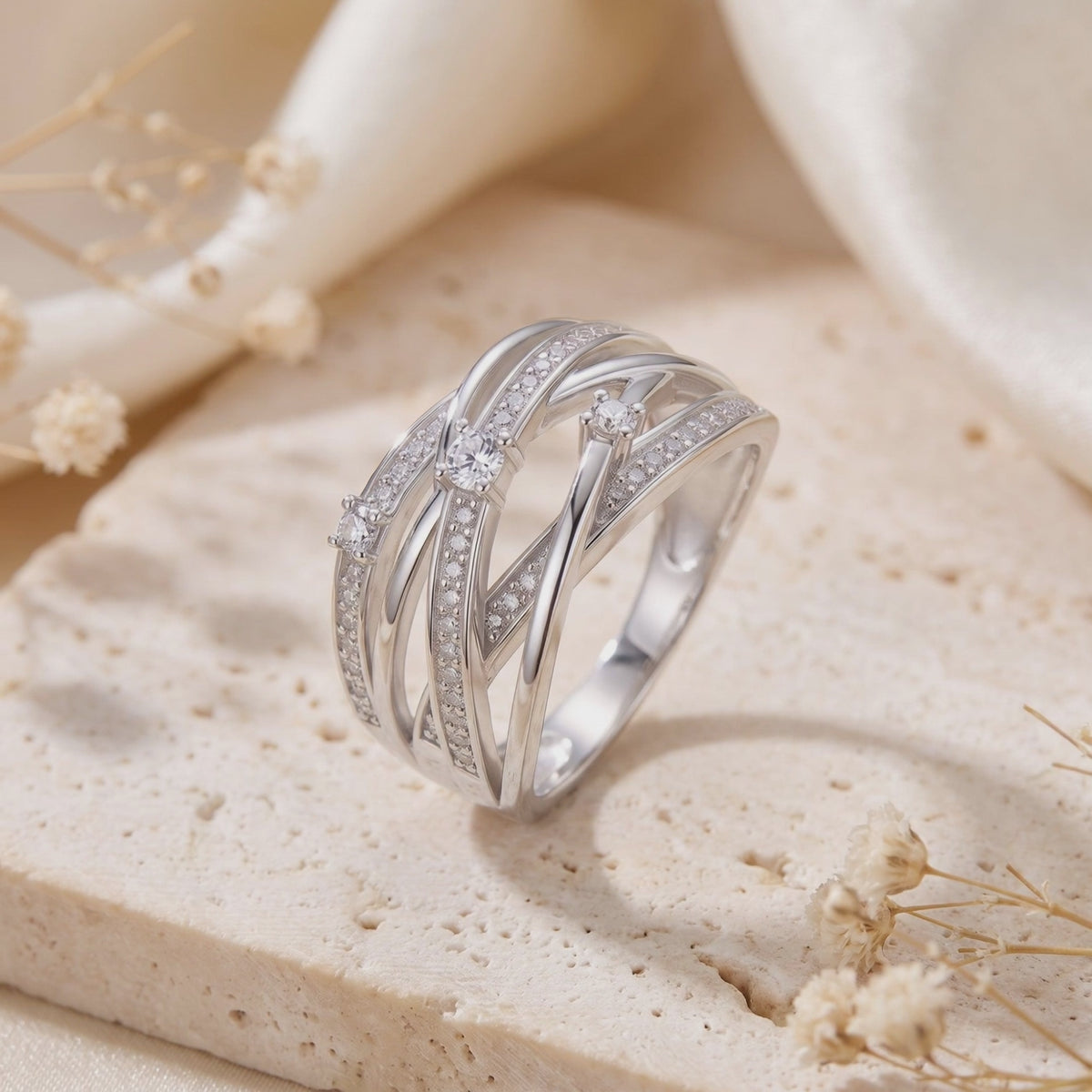Close-up of the multi-row silver crossover ring with cubic zirconia, resting upright on a beige textured block.