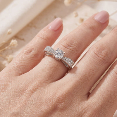 Silver bow ring with a round clear center stone, worn on a finger in a close-up view.