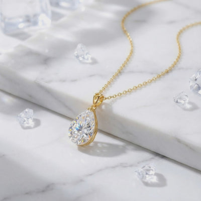 A solid gold necklace with a pear-cut A5 Zirconia pendant displayed on white marble among loose clear crystals.