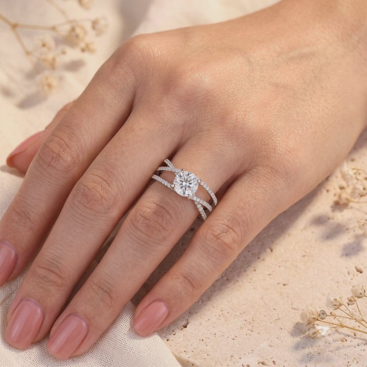 Silver criss-cross ring worn on a finger, with a round center stone and pavé-set overlapping bands.