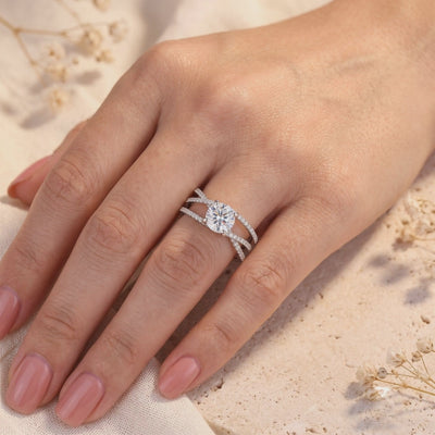 Silver criss-cross ring worn on a finger, with a round center stone and pavé-set overlapping bands.
