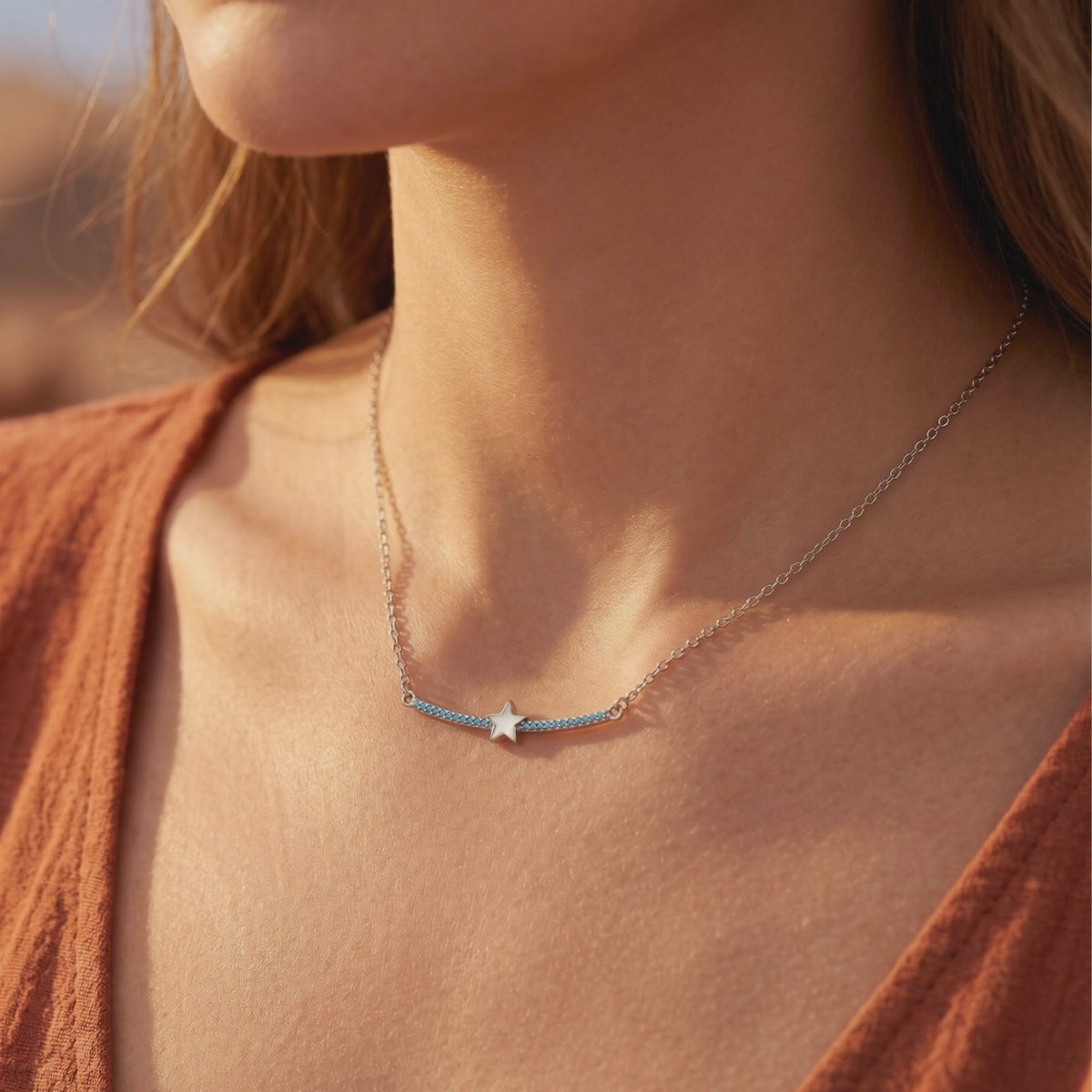 Silver star and turquoise bar necklace worn on a woman's collarbone against a rust-colored outfit.