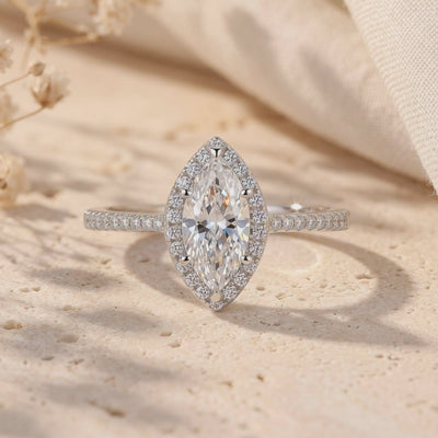 Front close-up of a silver marquise halo ring with a clear center gem on a textured stone surface.