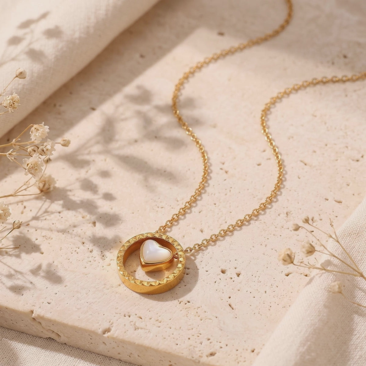 Gold-toned necklace with a mother-of-pearl heart inside a circular pendant, arranged on a textured stone surface.