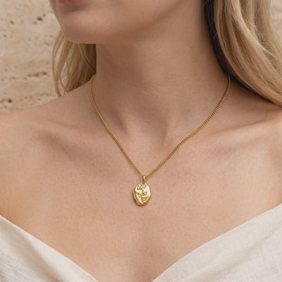 Model wearing a gold-tone necklace with a twisted chain and oval pendant etched with a rose motif.