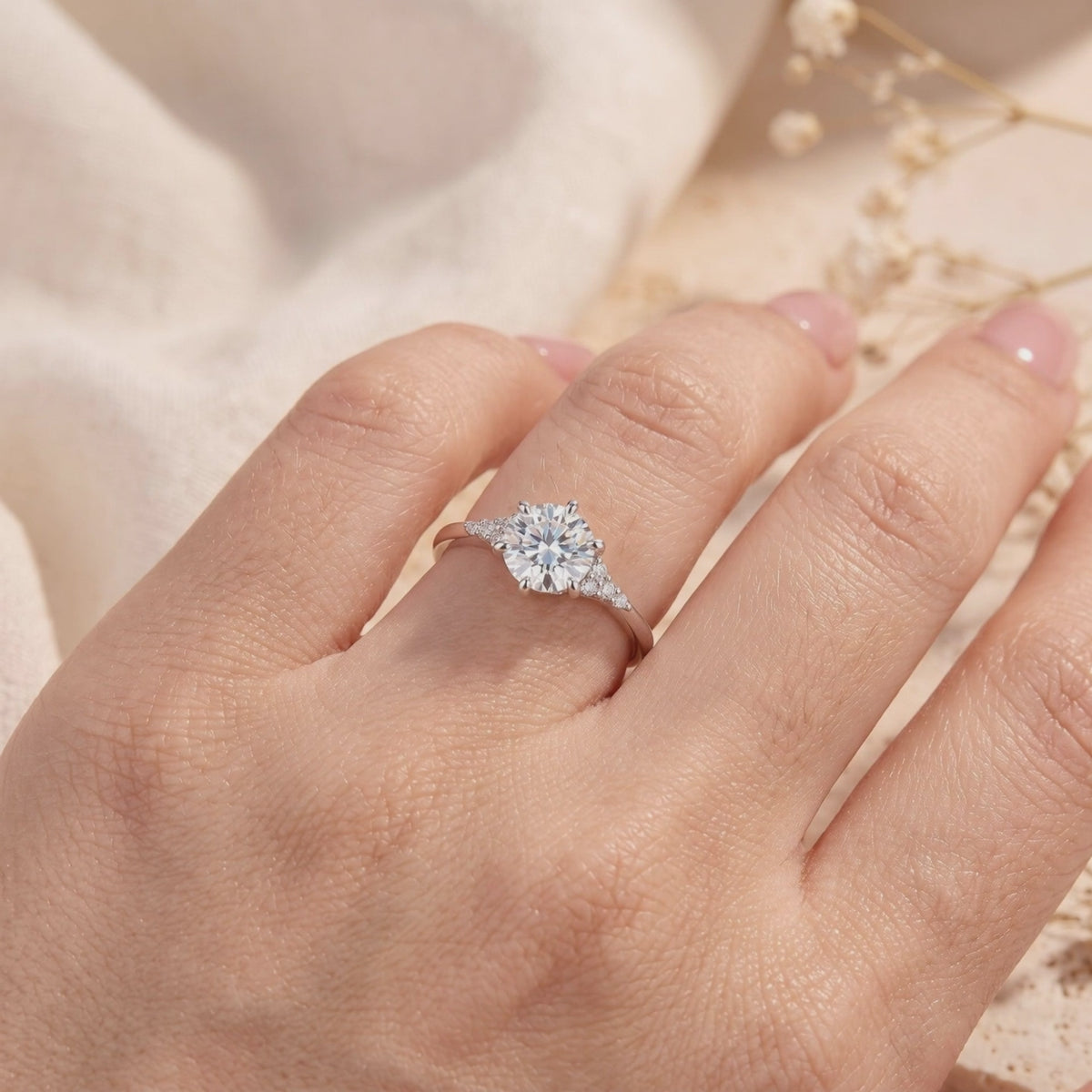 Silver ring with a round clear center stone and cluster accents, shown worn on a finger.