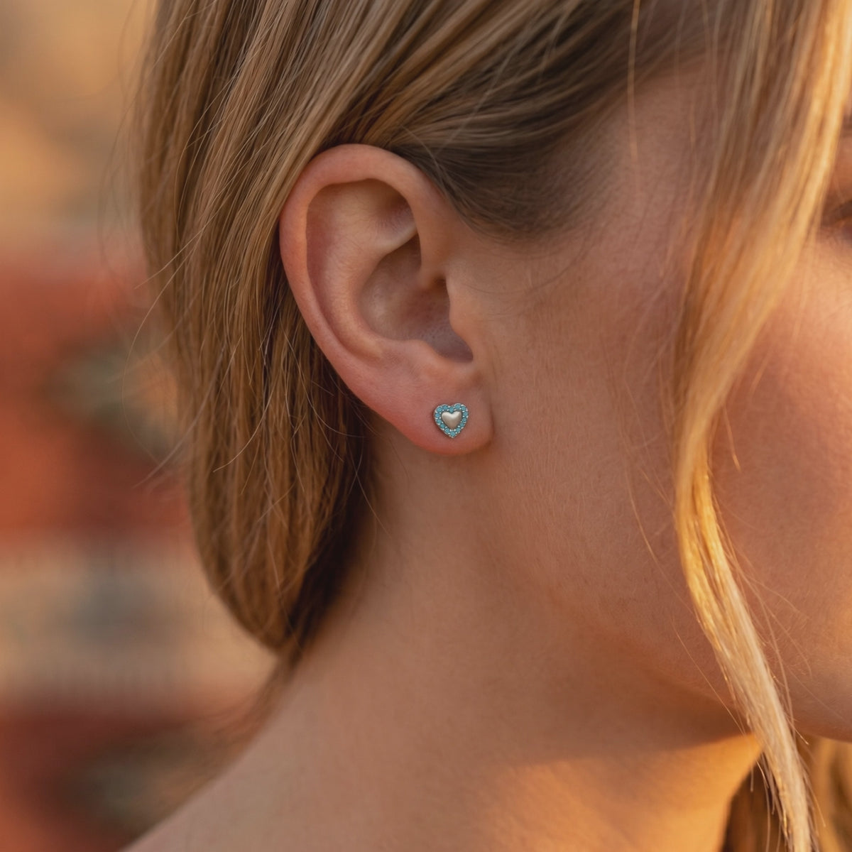 Close-up of a heart-shaped turquoise earring worn on an ear, with turquoise stones surrounding a light center.
