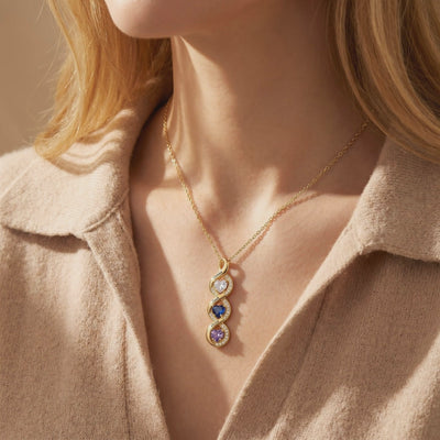 Model wearing a gold-toned vertical infinity pendant with three heart birthstones and engraved names.