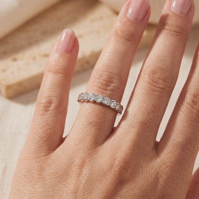 Silver bezel-set round clear-stone band worn on a hand against a warm beige background.