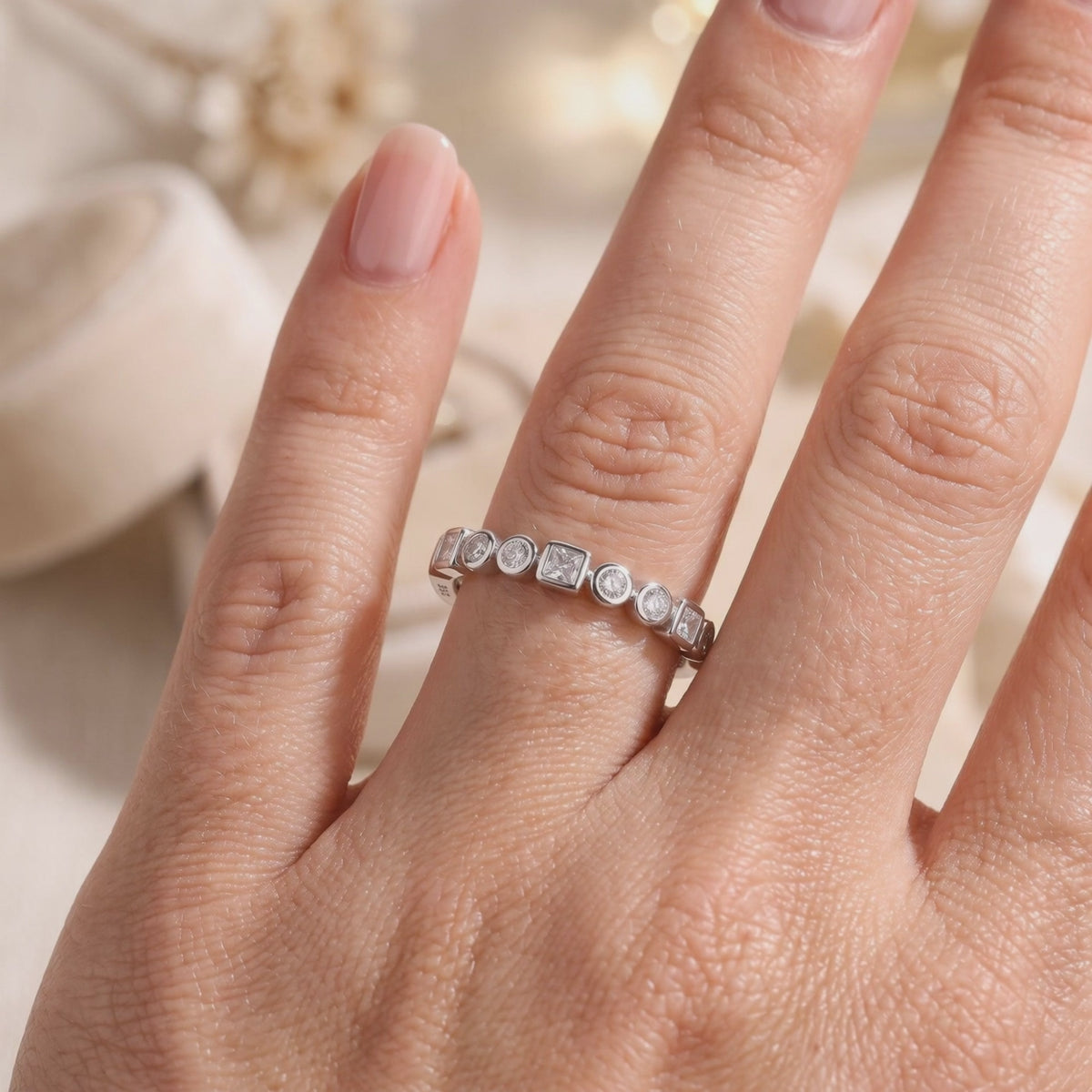 Silver ring with alternating round and square bezel-set clear stones worn on a finger.