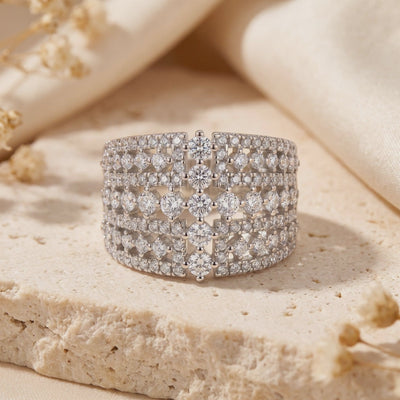 Front view of the wide silver Eleonora ring with a multi-row clear stone grid, resting on a textured stone surface.