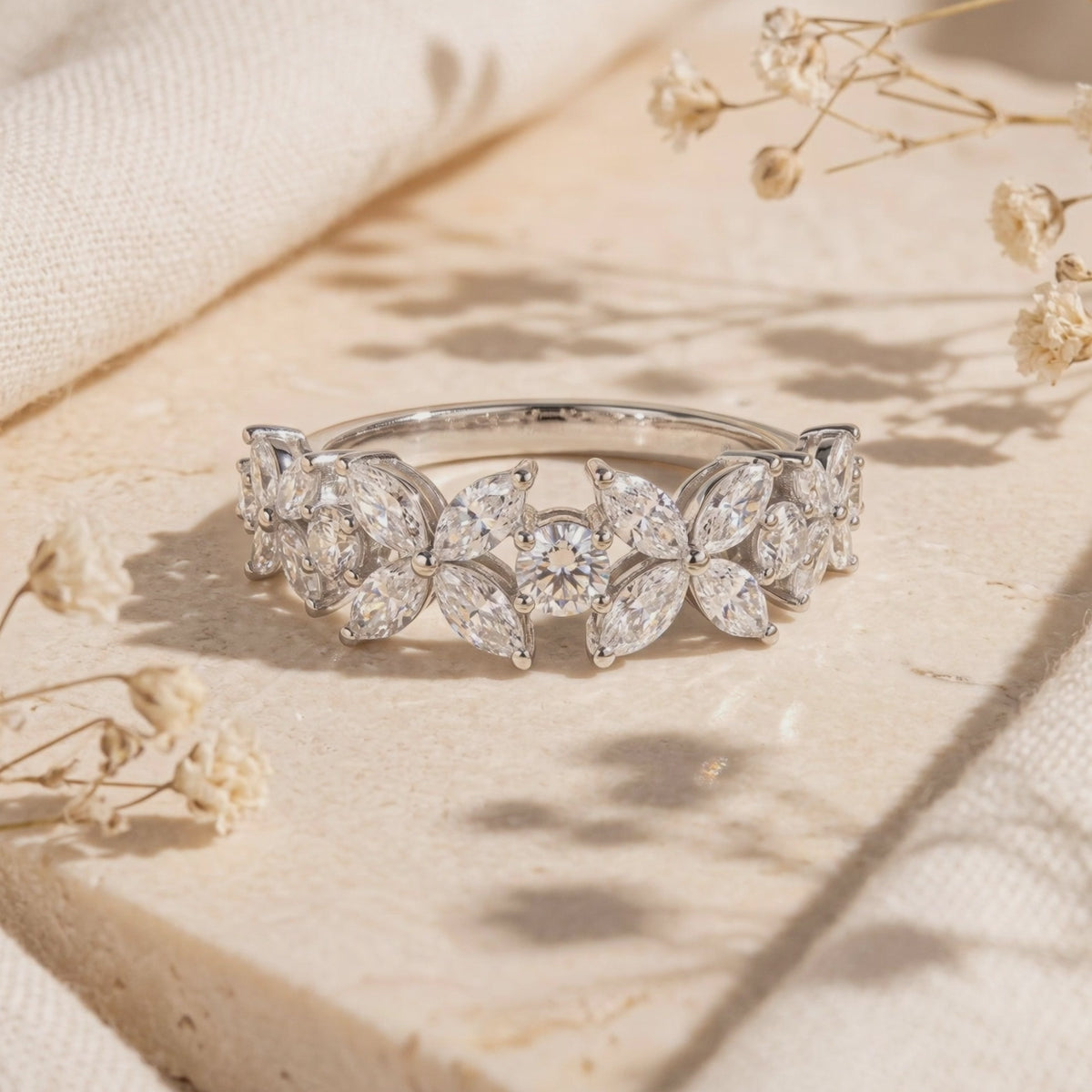 Close-up of the silver floral cluster ring with marquise stones displayed on a beige stone surface.