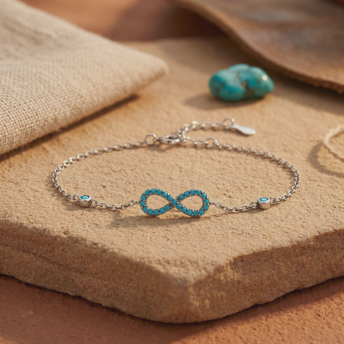 Silver turquoise infinity bracelet displayed flat on a tan stone slab with extender chain visible