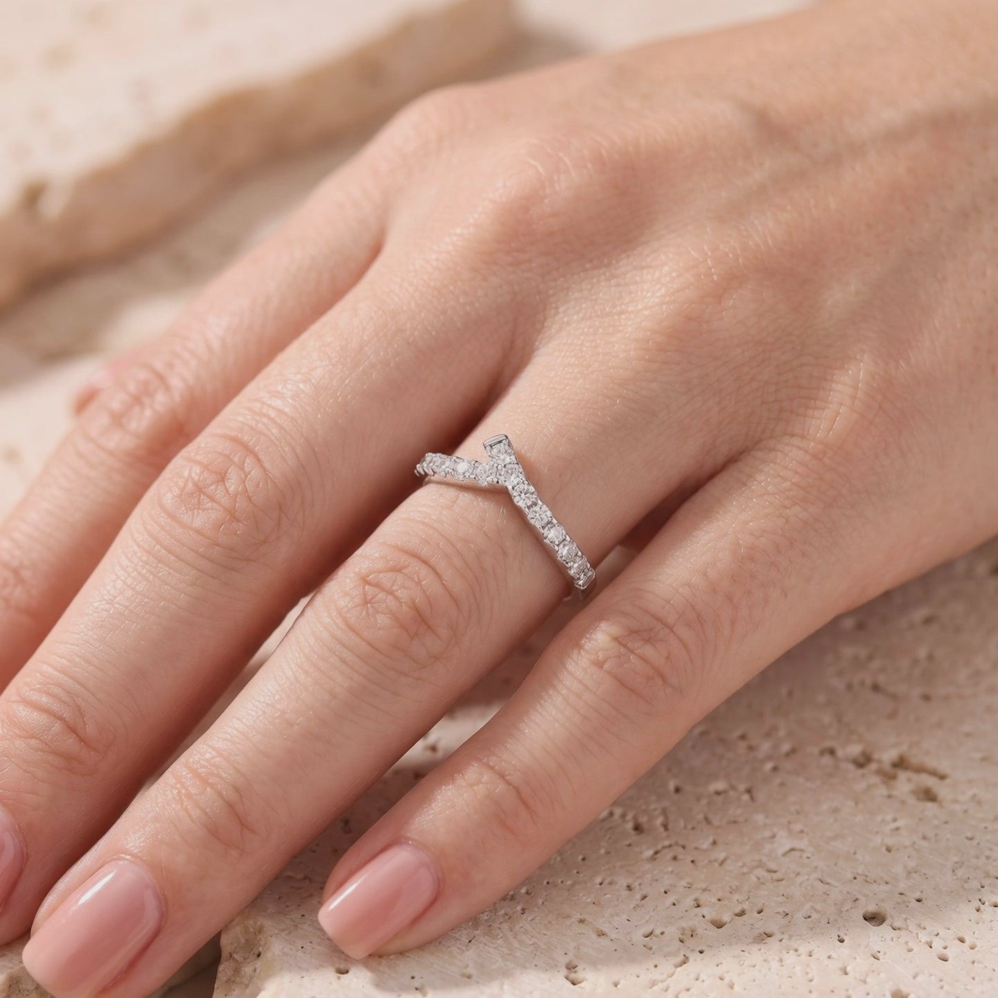 Silver asymmetric chevron ring with pave-set stones worn on a finger over a textured stone surface.