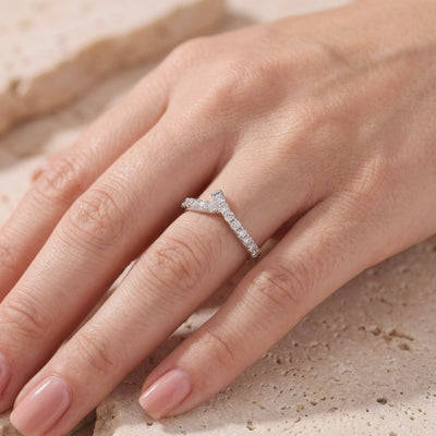 Silver asymmetric chevron ring with pave-set stones worn on a finger over a textured stone surface.