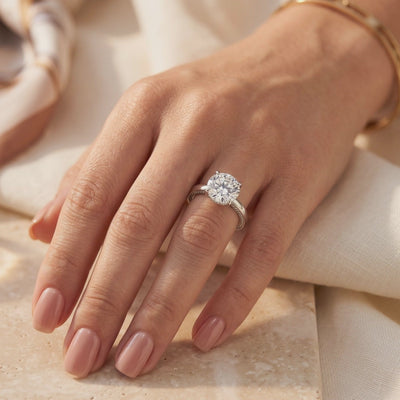 Silver solitaire ring with a large round-cut clear stone and pavé accents, worn on a hand.